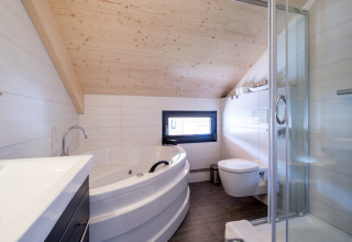 Modernes Badezimmer im Kreischberg Chalets 29 in Österreich mit Eckbadewanne, Glasdusche und schräger Decke.