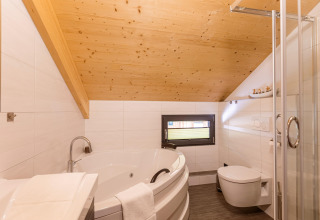 Modernes Bad mit Holzdecke, Eckbadewanne, Dusche und WC im Kreischberg Chalets 29 in Österreich.