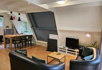 Stue i Chalet 'no 142' i Belgien med spisebord, sofa, tv og store skrå vinduer med udsigt til natur.