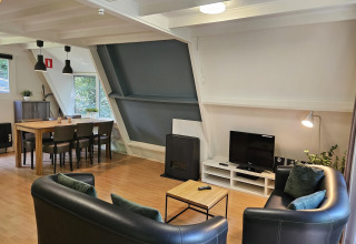 Wohnbereich im Chalet 'no 142' in Belgien mit Esstisch, Sofas, TV und großen Fenstern zur Natur.