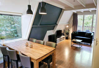 Modernes Wohnzimmer im Chalet Nr. 142 in Belgien mit Esstisch, Sofa, TV und Blick ins Grüne.