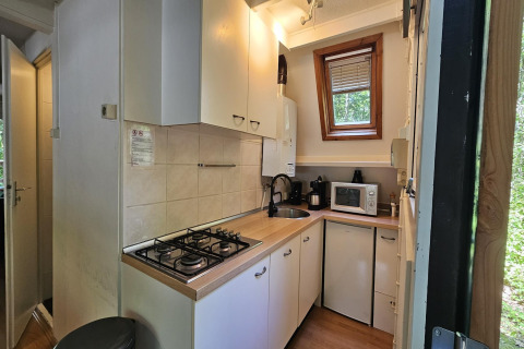Kleine Küche im Chalet 'no 142' in Belgien mit Gasherd, Spüle, Mikrowelle und Fensterblick.