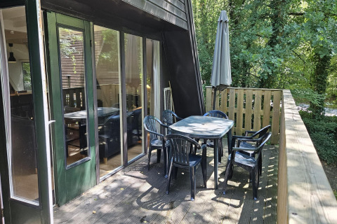 Balkon des Chalets „no 142“ in Belgien mit Gartentisch, sechs Stühlen und Sonnenschirm im Grünen.