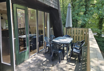 Balkon des Chalets „no 142“ in Belgien mit Gartentisch, sechs Stühlen und Sonnenschirm im Grünen.