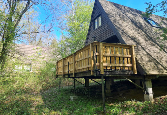 Ein A-Frame-Chalet mit Holzterrasse im Grünen bei Chalet Nr. 142 in Belgien, umgeben von Bäumen.