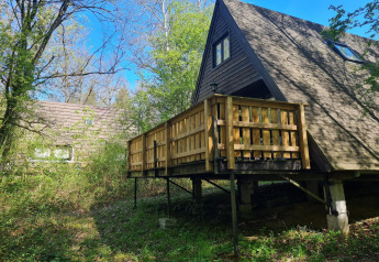 Ein A-Frame-Chalet mit Holzterrasse im Grünen bei Chalet Nr. 142 in Belgien, umgeben von Bäumen.