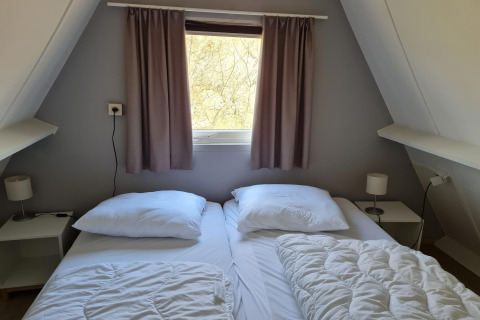 Gemütliches Schlafzimmer im Chalet Nr. 142 in Belgien mit zwei Betten, Fenster und Nachttischen.