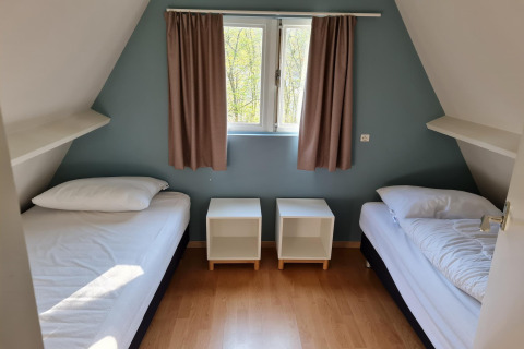 Schlafzimmer in Chalet 'no 142' in Belgien mit zwei Einzelbetten, Nachttischen und Fenster mit Vorhängen.