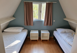 Schlafzimmer in Chalet 'no 142' in Belgien mit zwei Einzelbetten, Nachttischen und Fenster mit Vorhängen.