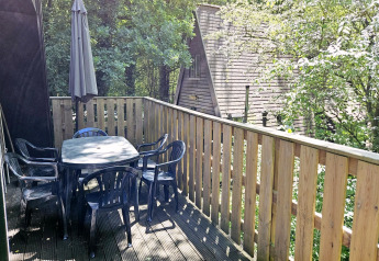 Terrasse von Chalet Nr. 142 in Belgien mit Tisch, Stühlen, Sonnenschirm und grüner Waldkulisse.