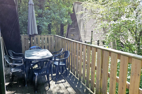 Terrasse von Chalet Nr. 142 in Belgien mit Tisch, Stühlen, Sonnenschirm und grüner Waldkulisse.