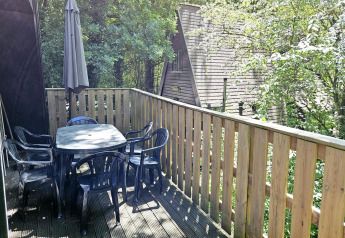 Terrasse von Chalet Nr. 142 in Belgien mit Tisch, Stühlen, Sonnenschirm und grüner Waldkulisse.