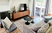 Modernes Wohnzimmer im Chalet Nr. 186 in Belgien mit Sofa, Sessel, TV, Tischen und Terrasse.