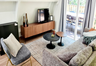 Modernes Wohnzimmer im Chalet Nr. 186 in Belgien mit Sofa, Sessel, TV, Tischen und Terrasse.