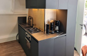 Moderne tekøkken i Chalet no 186 i Belgien med sort indretning, kaffemaskiner og gaskomfur.