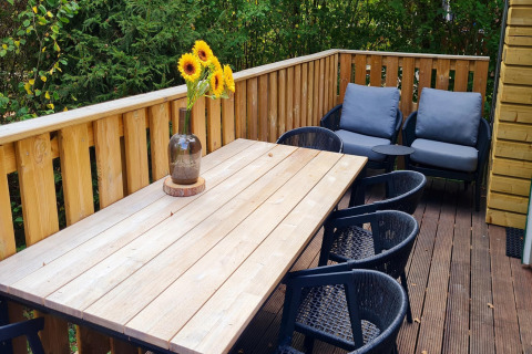 Terrasse des Chalets 'no 186' in Belgien mit Holztisch, Stühlen, Sonnenblumen und Loungesesseln.