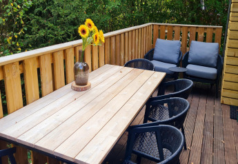 Terrasse des Chalets 'no 186' in Belgien mit Holztisch, Stühlen, Sonnenblumen und Loungesesseln.