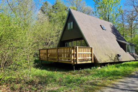 A-förmiges Chalet Nummer 186 in Belgien, umgeben von üppigem Grün und Bäumen bei sonnigem Wetter.