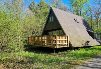 A-förmiges Chalet Nummer 186 in Belgien, umgeben von üppigem Grün und Bäumen bei sonnigem Wetter.