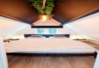Modernes Schlafzimmer im Chalet no 186 in Belgien mit großem Bett, Schrägdach und hängendem Pflanzenlicht.