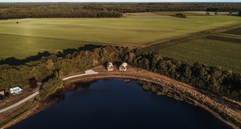 Luftfoto af vandhytter ved en sø i Rekreativt park De Achterste Hoef, omgivet af grønne marker i Holland.