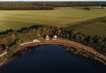Vue aérienne de cabanes au bord d’un étang au parc De Achterste Hoef, entouré de champs aux Pays-Bas.