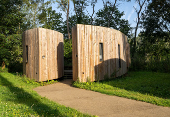 Hébergement glamping moderne avec deux cabanes en bois incurvées entourées de verdure et d'arbres.