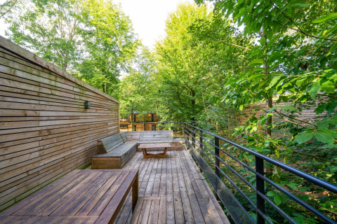 Houten terras met zithoek bij The Cottage by YourNature, omringd door weelderig groene bomen.