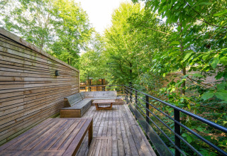 Terraza de madera con bancos en The Cottage by YourNature, rodeada de frondosos árboles verdes.