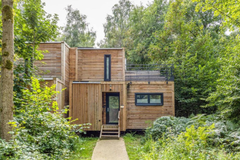 Modern houten huisje bij The Cottage by YourNature, gelegen in het bos en omringd door groene bomen.