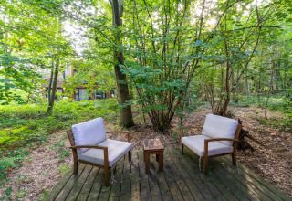 Zona de descanso con dos sillas y mesa sobre tarima de madera en el bosque junto a The Cottage, YourNature.