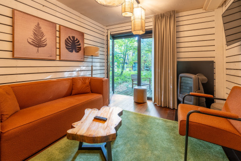 Acogedora sala de glamping en The Cottage by YourNature con sofás naranjas y vistas al bosque exterior.