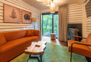 Acogedora sala de glamping en The Cottage by YourNature con sofás naranjas y vistas al bosque exterior.