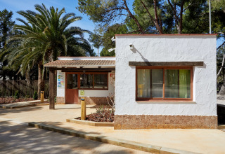 Eingang zum TAIGA Lake Caspe Ferienpark in Aragón, Spanien, umgeben von Palmen und Bäumen.