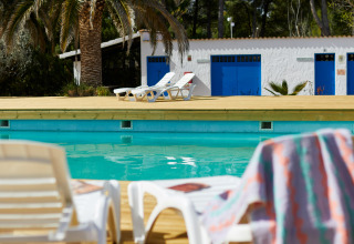 Poolside at TAIGA Lake Caspe holiday park in Aragón, Spain, with sun loungers, palm trees, and white buildings.