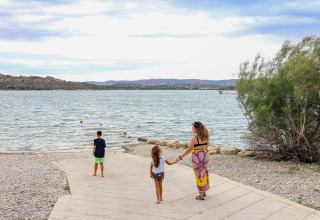 Una mujer y dos niños caminan hacia el agua en el parque vacacional TAIGA Lake Caspe en Aragón, España.