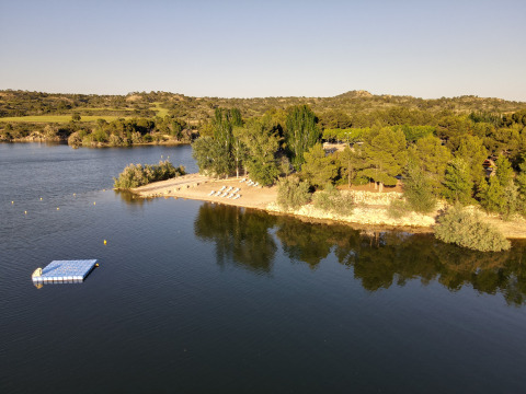 Vista aérea de la playa y embarcadero flotante en TAIGA Lake Caspe, rodeado de árboles en Aragón, España.