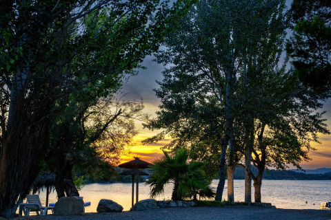 Sunset over the lake at TAIGA Lake Caspe holiday park in Aragón, Spain, with trees framing the tranquil water.