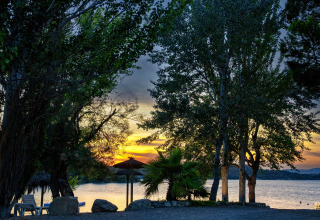 Sunset over the lake at TAIGA Lake Caspe holiday park in Aragón, Spain, with trees framing the tranquil water.