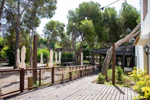 Sunny outdoor terrace with bar stools and string lights at TAIGA Lake Caspe holiday park in Aragón, Spain.