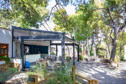 Terrasse ombragée d'un café avec tables, chaises et arbres au parc TAIGA Lake Caspe en Aragon, Espagne.
