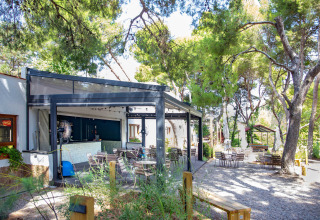 Outdoor seating at a shaded café surrounded by trees at TAIGA Lake Caspe holiday park in Aragón, Spain.