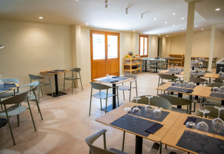Moderne restaurantinteriør på TAIGA Lake Caspe-feriepark i Aragón, Spanien, med dækkede borde og stole.