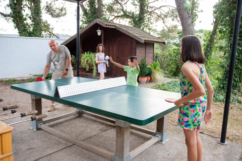 Famiglia che gioca a ping pong all’aperto al parco vacanze TAIGA Lake Caspe in Aragona, Spagna, vicino a una baita.
