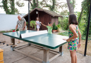 Famiglia che gioca a ping pong all’aperto al parco vacanze TAIGA Lake Caspe in Aragona, Spagna, vicino a una baita.