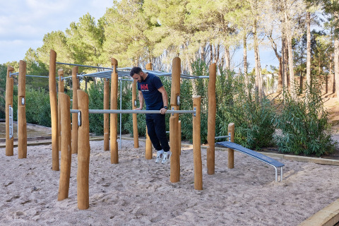 Uomo che si allena alle barre fitness esterne nel parco vacanze TAIGA Lake Caspe in Aragona, Spagna, tra gli alberi.