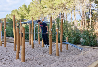 Uomo che si allena alle barre fitness esterne nel parco vacanze TAIGA Lake Caspe in Aragona, Spagna, tra gli alberi.