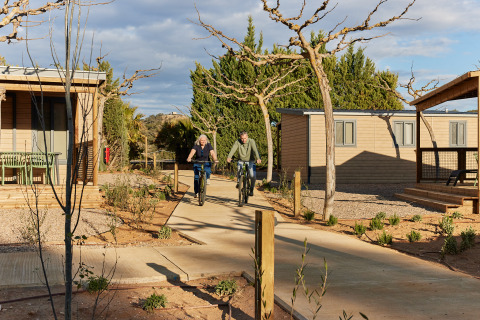 Due persone vanno in bicicletta nel villaggio turistico TAIGA Lake Caspe in Aragona, Spagna, tra le cabine.