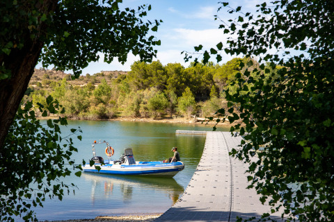 Barca ormeggiata a un pontile galleggiante nel parco vacanze TAIGA Lake Caspe, circondato da alberi in Aragona, Spagna.
