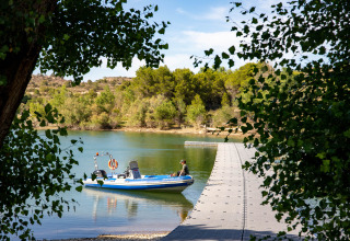Barca ormeggiata a un pontile galleggiante nel parco vacanze TAIGA Lake Caspe, circondato da alberi in Aragona, Spagna.